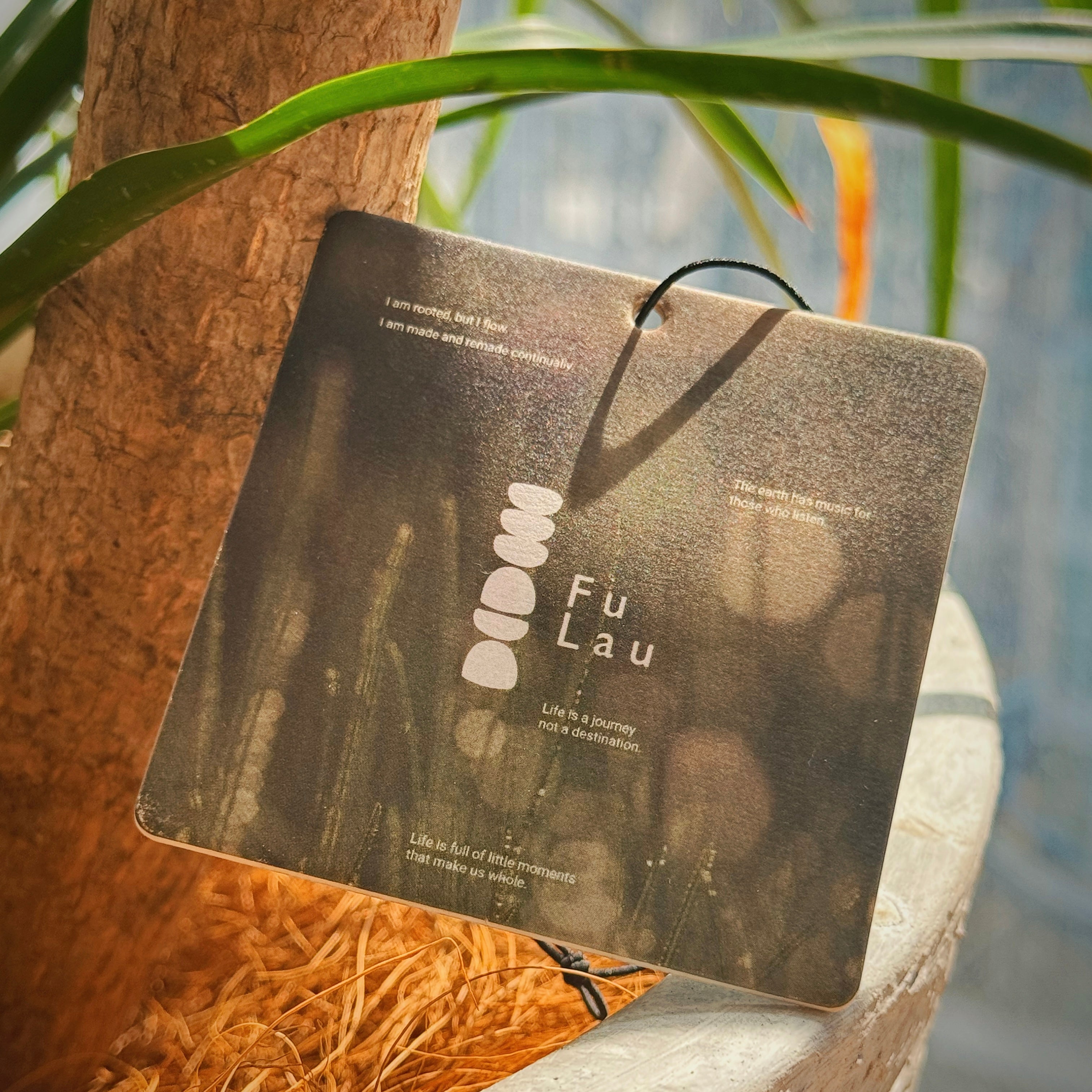 A FuLau portable scent card hanging near green leaves